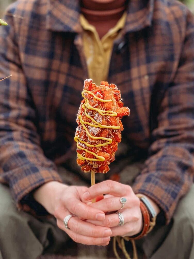 Hands holding a Korean corn-dog on a stick, from Manna Seoul